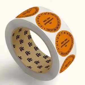 NEN 1004 keuringssticker op rol - rond - oranje zwart - tekst NEN 1004 goedgekeurd tot met jaartallen 26-31 en maanden